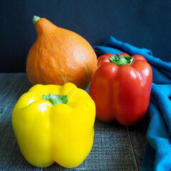 Wall Mural - yellow and red bell peppers and orange pumpkin stand side by side on a dark background with a blue cloth . autumn vegetables