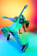 Wall Mural - Close-up two hip-hop dancers, stylish emotive girl and boy in action and motion in casual sports youth clothes on gradient multi colored background at dance hall in neon light.