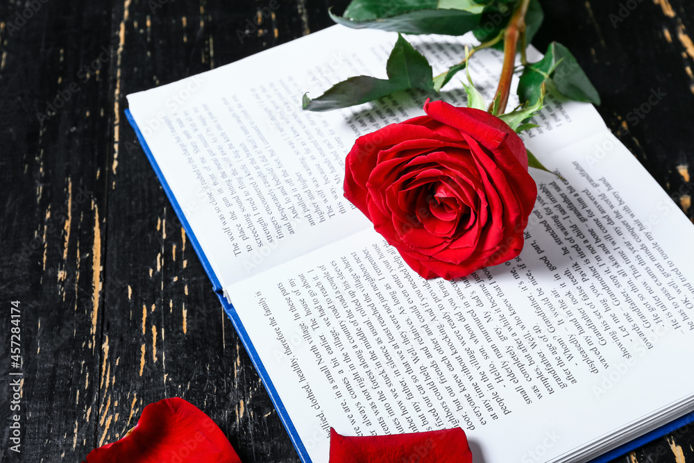 Opened book and beautiful rose on dark wooden table