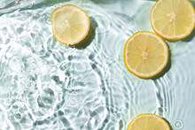 Fresh Pieces Of Lemon And Clean Blue Water,bright Sunlight.Empty Space.Lemons And Splashing Water As A Background