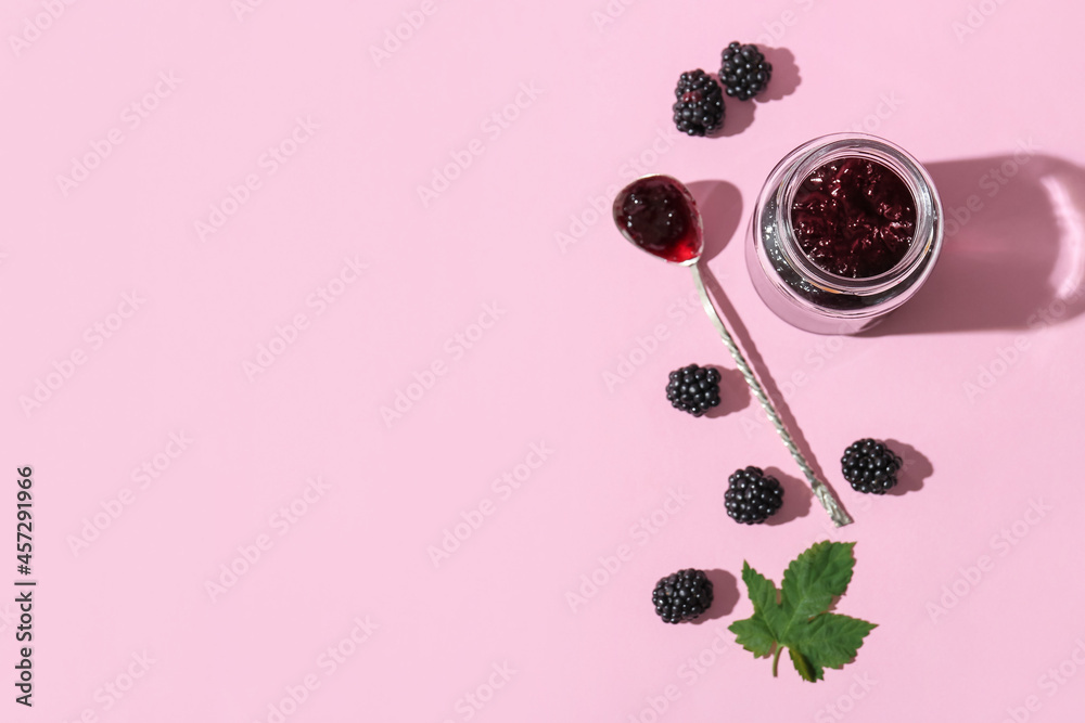 Jar and spoon with tasty blackberry jam on color background