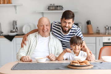 Poster - Happy man, his little son and father having breakfast in kitchen