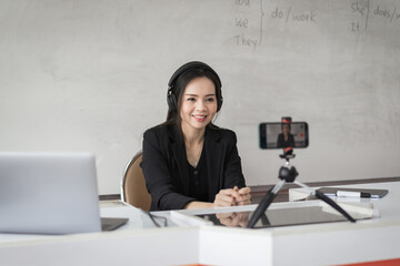 Adult Asian female college teacher teaching online via video conference meeting to students at home. Smiling Asian female tutor having a video call with students