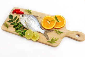 Gerres Fish (Gerres Filamentosus) , Whipfin silver biddy Fish , Decorated with curry Leaves and Tomato on a Wooden pad,White Background.Selective focus.