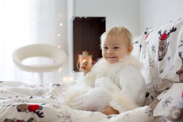 Canvas Print - Adorable little baby boy in handknitted overall, eating cookies in bed on Christmas