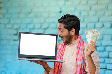 Wall Mural - Young indian farmer showing laptop screen and money