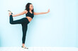 © halayalex - Portrait of fitness smiling black woman in sports clothing with afro curls hairstyle.She wearing sportswear.Young beautiful model stretching out before training.Female posing in studio near blue wall