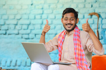 Wall Mural - Indian farmer using laptop and showing thumps up at home.