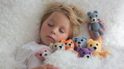 Canvas Print - Little toddler child, cute blond boy, lying down in bed with many teddy bears, handmade amigurumi toys at home.