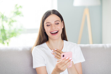 Wall Mural - Portrait of attractive cheerful girl sitting on divan using device reading funny post smm laughing resting at home indoors