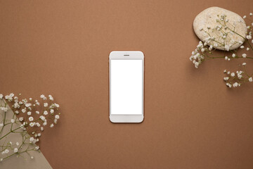 Mobile phone with white screen and dry flower branch and stone on a light brown background. Trend, minimal concept with copyspace