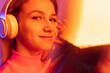 © Lustre Art Group  - Close-up image of young beautiful girl listening to music in headphones isolated over gradient background in neon lights. Bokeh effect