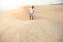 Young Male With Curly Hair, Walking On Sand Dunes During Golden Hour