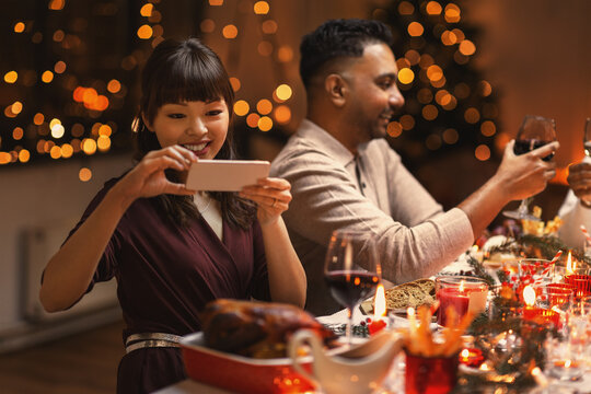 holidays, party and celebration concept - happy smiling asian woman having christmas dinner with friends and photographing food at home