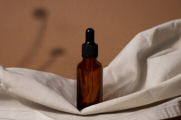 Creative photo of cosmetic bottle with pipette on beige fabric and brown background with shadow of tropical flower. Advertising