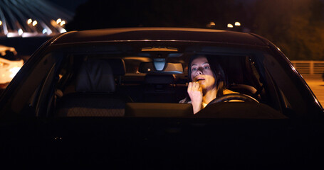 Woman driver sitting in car doing make up using lipstick.