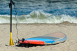 Closeup of lone paddleboard laying in the sand with paddle stuck in the sand with rolling ocean waves in background