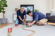 Senior father and adult son playing with toy wooden together at home with happy and smile. Two men playing with toy car on floor in living room