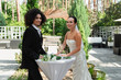 Smiling interracial lesbian couple standing near bouquet and champagne during wedding outdoors.