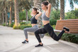 Two sporty women doing lunge step over bench outdoors.