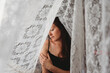 © Cavan Images - Beautiful woman with long brown hair surrounded by lace curtains.