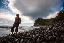 Female Hiker With Backpack On Pololu Beach, Hawaii Looks At Pacific.