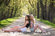 © Cavan Images - Two pretty teen girls sitting on a tree lined country road.