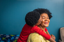 Grandson Kissing Grandmother On Cheek By Blue Wall At Home