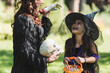 © LIGHTFIELD STUDIOS - blurred woman in black halloween costume scaring cheerful daughter with toy hand