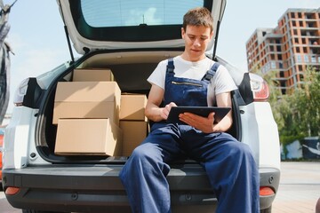 Young male courier with parcels near delivery service car