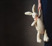 Cropped Image Of Child's Hand Holding Stuffed Rabbit Against Dark Wall