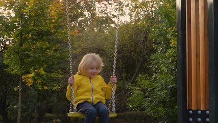 Wall Mural - Little boy having fun on a swing on the playground in public park on autumn day. Happy child enjoy swinging. Active outdoors leisure for child in city