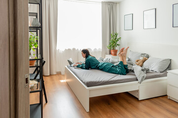 Young woman work at laptop while sitting on bed in bedroom. Concept of remote work. Wellness and mental health concept