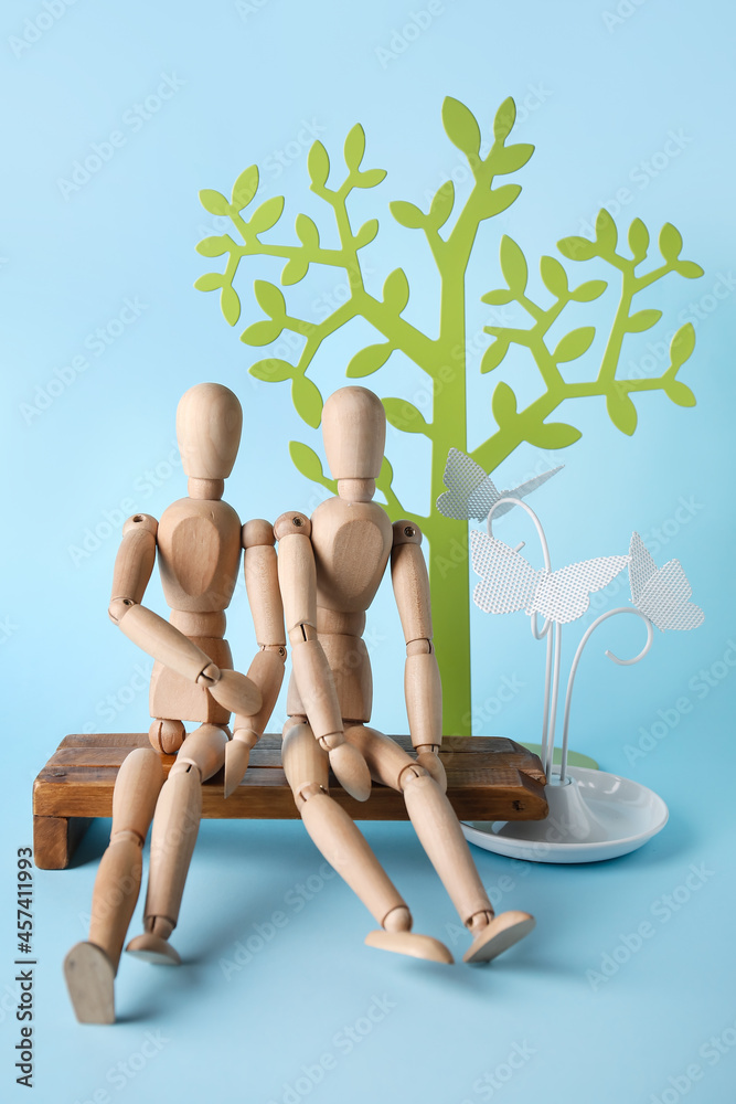 Wooden mannequins sitting on bench on color background