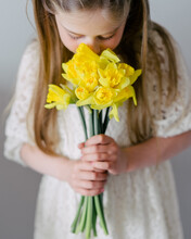 A Young Girl Sniffs The Beautiful Yellow Flowers Of Narcissus. Spring