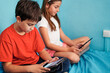 © Cavan Images - Boy and girl sitting on bed looking at tablet in room at home