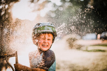 Young Boy Playing Outside In Sprinkler Splashing Water And Laughing