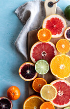 Slices Of Various Citrus Fruit On Cutting Board On Blue Background.