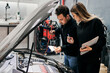 © Cavan Images - Male mechanic teaches female mechanic how to fix a vehicle