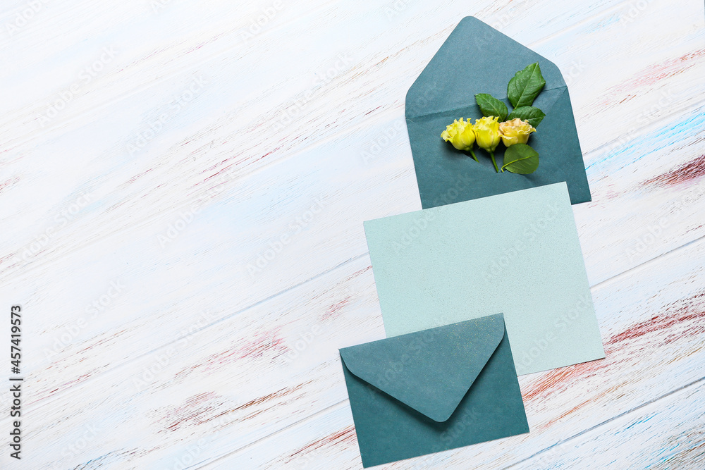 Blank card with envelopes and roses on white wooden background
