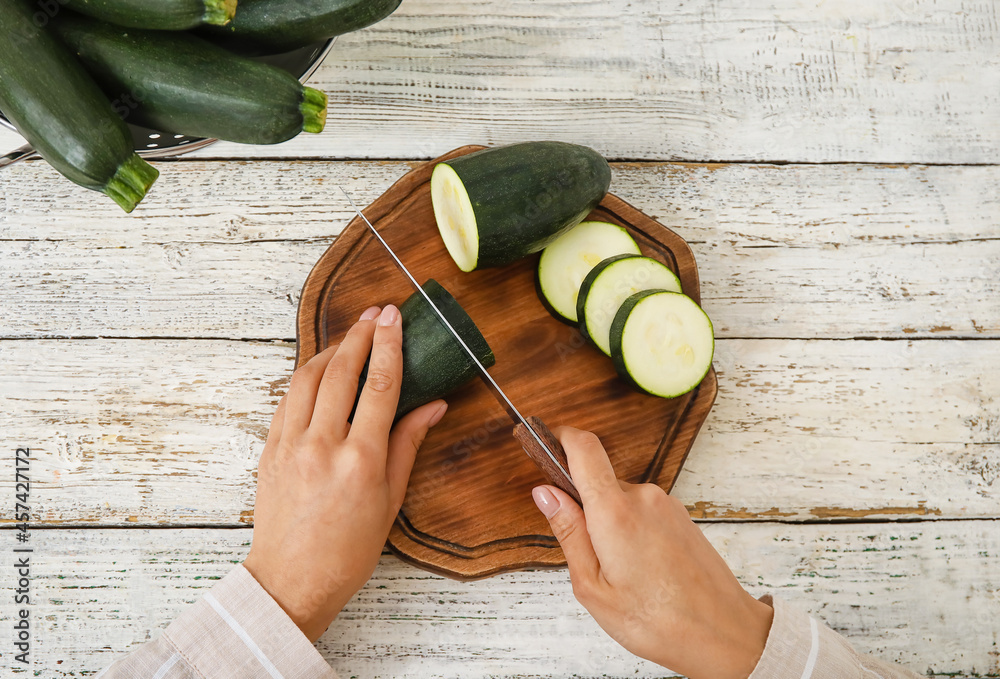 Woman cutting fresh zucchini squash on light wooden table
