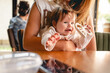 © Miljan Živković - Close up on small happy caucasian baby girl or boy infant smiling in hands of her mother sitting by the table at restaurant or cafe in bright day childhood and growing up concept real people