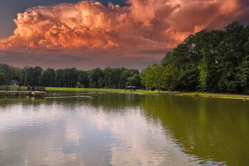 a gorgeous shot of still silky green lake water surrounded by lush green trees with powerful clouds in the sky at Huddleston Pond Park in Peachtree City, Georgia