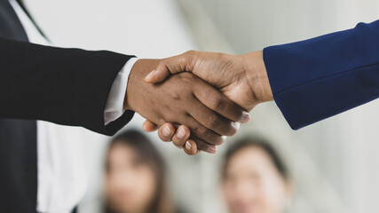 Wall Mural - Selective focus on business women's hands in formal suits doing hand shake during business meeting with blurry colleagues in background. Concept for business meeting