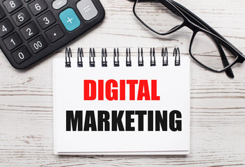 Fototapete - On a light wooden table calculator, glasses and a blank notepad with the text DIGITAL MARKETING. Business concept