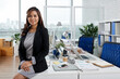 © DragonImages - Portrait beautiful elegant business lady sitting on office desk and smiling at camera