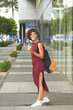 Attractive happy young woman walking outdoors with big backpack, shopping bags and refreshing drink
