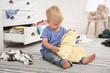 © New Africa - Cute little boy playing with clothes near dresser on floor at home