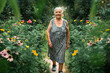 Portrait of a very old woman walking in her garden  with flowers in summer. Grandparents day. Hobbies for the elderly concept.