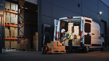 Outside Of Logistics Distributions Warehouse Delivery Van: Worker Unloading Cardboard Boxes On Hand Truck, Online Orders, Purchases, E-Commerce Goods, Food, Medical Supply. Evening Shot